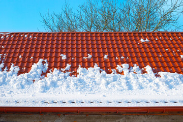 Snow melts from the roof of the house on a spring day. Danger of avalanches from roofs. Snow removal