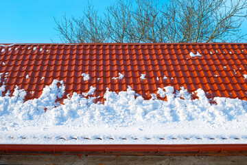 Naklejka premium Snow melts from the roof of the house on a spring day. Danger of avalanches from roofs. Snow removal
