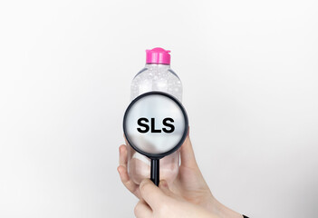 A woman examines the harmful ingredients of the micellar waterthrough a magnifying glass. Means with SLS. The concept of hazardous substances in cosmetics and household chemicals