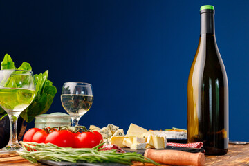 Bottle of wine with cut cheese and tomatoes against blue background