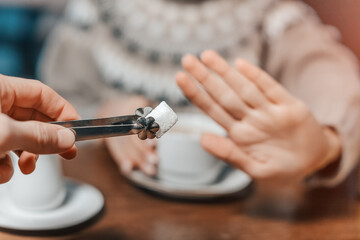 Woman in a cafe refuses a piece of white sugar for her tea. Say no to sugar and fast carbs. Diet for diabetes and addiction to sweet junk food