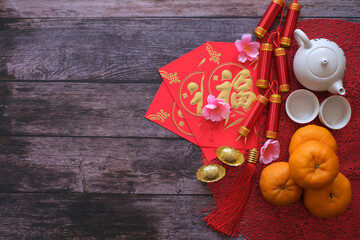 Chinese New Year festival concept. Mandarin oranges, red envelopes, gold ingots and tea pot on red cloth with old wooden background. Chinese characters mean rich, wealthy, healthy and happy.