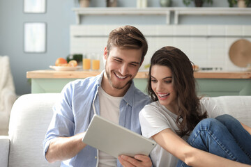 Young couple watching media content online in a tablet sitting on a sofa in the living room.
