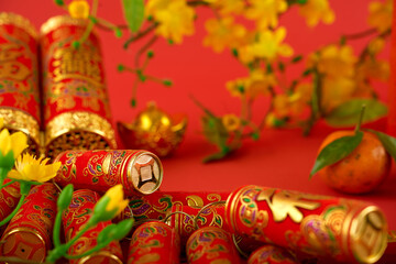 Red firecrackers with best wishes inscriptions, apricot flowes and tangerines on red table prepared for Chinese New Year celebration