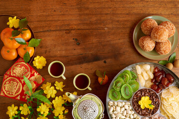 Wooden table prepared for Chinese New Year with tea cups, box of dried fruits and nuts, fried rice balls and greeting cards with best wishes inscription, view from the top
