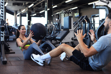 Fit and muscular couple exercising with medicine ball at gym.