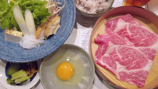 Japanese Sukiyaki hot pot with raw egg, sliced beef meat,tofu curdled soy milk, negi welsh onion,shungiku crown daisy,gobou greater burdock,shirataki konjac,fu wheat gluten,enoki mushrooms and rice.