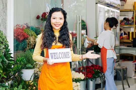Beautiful young Vietnamese woman holding welcome sign when standing at entranse of family flower shop