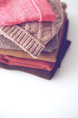 Stack of cozy knitted sweaters on white background. Autumn-winter concept.