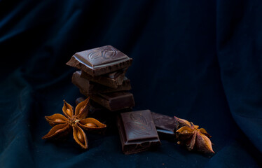 Broken pieces of dark chocolate and chocolate chips on a black background. Copy the space.