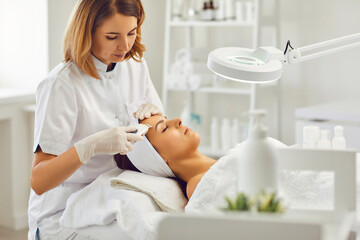 Female beautician makes a procedure for ultrasonic skin cleansing of a young patient in a beauty...
