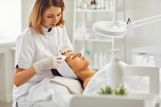 Female beautician makes a procedure for ultrasonic skin cleansing of a young patient in a beauty spa.