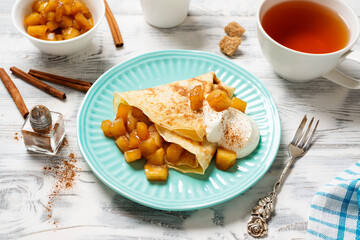 Crepes, thin pancakes with caramelized apple filling and cream fresh. Healthy breakfast in sunny...