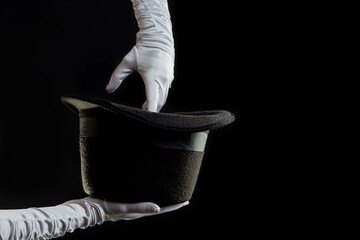 Hand gestures. Showman shows disappearing tricks in a hat, white gloves and black top hat, black background