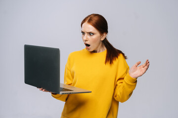 Shocked young business woman or student with opened mouth holding keeping opened laptop computer...