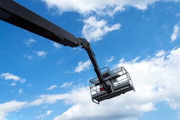 Hydraulic lifting platform with a bucket on a blue, cloudy sky. Building. Industry. Construction machinery.