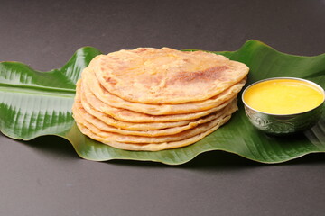 Puran Poli, also known as Holige, is an Indian sweet flatbread from India consumed mostly during Holi festival. Served on banana leaf with pure Ghee over black background.