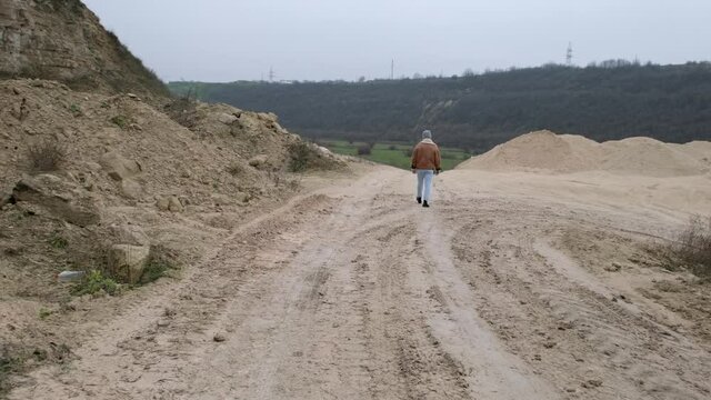 A young guy in a jacket and jeans walks along an abandoned stone carier