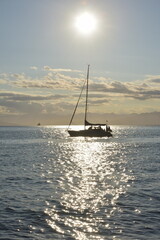 Silhouette of yacht with people crossing sun reflection in sea water, sun shining above. Expedition to the Kuril islands to the south from Kamchatka peninsula.