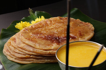 Puran Poli, also known as Holige, is an Indian sweet flatbread from India consumed mostly during Holi festival. Served on banana leaf with pure Ghee over black background.