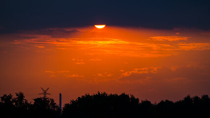 Landscape silhouettes at sunset with sun disk behind dark clouds