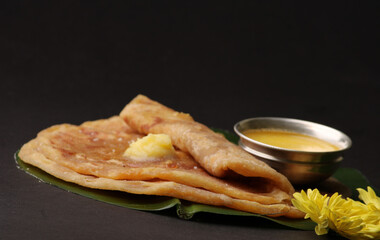Puran Poli, also known as Holige, is an Indian sweet flatbread from India consumed mostly during Holi festival. Served on banana leaf with pure Ghee over black background.
