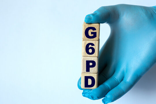 G6PD is an acronym on cubes held by a hand in a blue glove