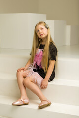 Cute little girl is sitting in the studio on the white stairs. style and fashion concept, happy childhood.