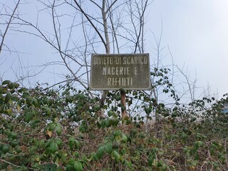 Green shrubs and old italian sign with writings against garbage abandonment