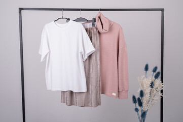 Women's minimal fashion pastel clothes. Stylish female t-shirts, hoodie, pants on hanger on white background. Fashion blog, website, social media hero header.
