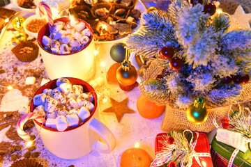 Fototapeta premium sweet food top view background for merry christmas or new year holiday decoration with night illumination - chocolate candies, tangerines, cookies, marshmallow and cocoa latte on white wood