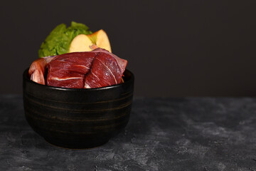 Bowl with mixture of biologically appropriate raw dog food containing meat chunks, fish, fruits and vegetables on dark background with copy space