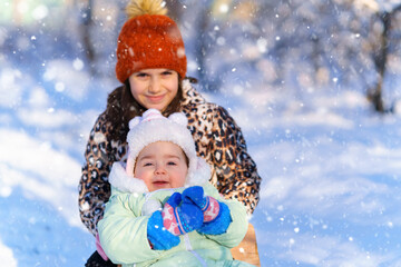 children sitting on sledge in the winter forest and playing, bright sunlight and shadows on the snow, beautiful nature