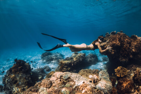 Freediving underwater in blue ocean. Woman freediver with fins and corals.