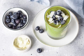 chia pudding with green superfood powder, banana, almond milk topped with blueberries and coconut chips. healthy superfoods breakfast concept. Gray background. close-up, top view