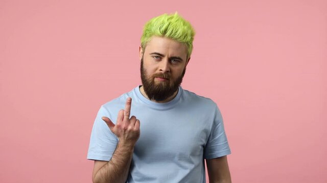 Rude impolite bearded man with dyed bright green hair showing middle finger fuck gesture at camera, conflict situation, negativity. Indoor studio shot isolated on pink background
