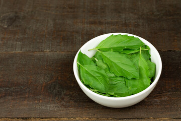 Tulsi or Holy basil leaf in white bowl on wooden background. Tulsi is used in ayurvedic medicine.