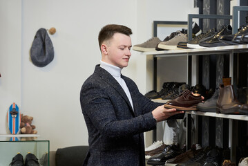A young man in a white turtleneck sweater and a suit is evaluating shoes in a clothing store. A male customer in a shoe boutique.