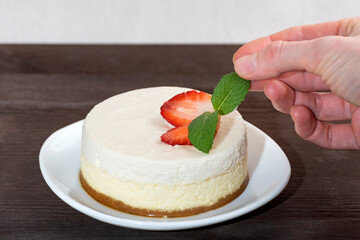 Cheesecake cake with fresh strawberries on white plate. Woman's hand decorated cake a mint