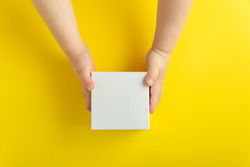 White cardboard box in children's hands, yellow background. Top view. Copy space, mock up.