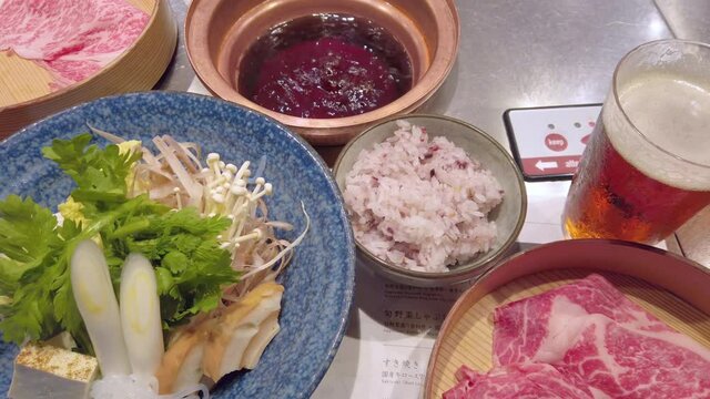 Japanese Sukiyaki hot pot with raw egg, sliced beef meat,tofu curdled soy milk, negi welsh onion,shungiku crown daisy,gobou greater burdock,shirataki konjac,fu wheat gluten,enoki mushrooms and rice.