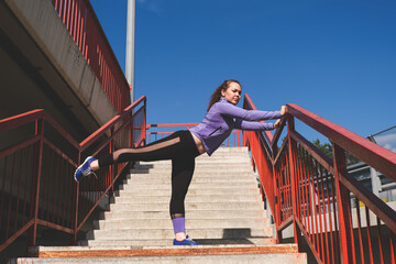 young athletic girl stands with her foot on the railing of the stairs, workout urban sport concept