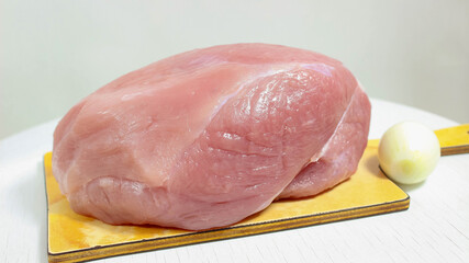 Raw pork tenderloin on a chopping board close-up with onion and garlic.