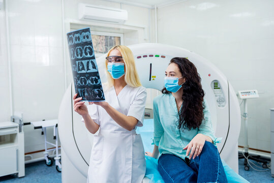 Radiologist with a female patient wearing protective masks examining a CT scan