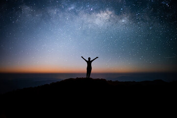 Silhouette of young traveler watched the star and milky way on top of the mountain alone before sunrise. He raised his arms over his head, expressing his joy and success, and enjoyed his hike.