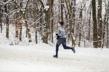 Fast runner running in forest on snowy winter day. Healthy lifestyle, winter fitness