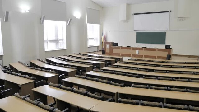 Empty modern lecture auditorium, conference hall with tribune, microphone, white screen, projector, rows desks