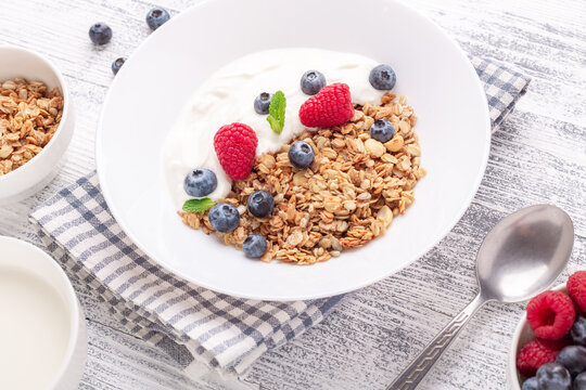 Homemade granola with yogurt and fresh berries in white ceramic plate on wooden background - Image