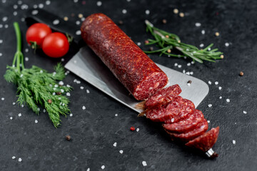 salami sausage on a knife with fresh rosemary and spices on a stone background