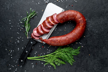 smoked sausage on a knife with spices on a stone background with copy space